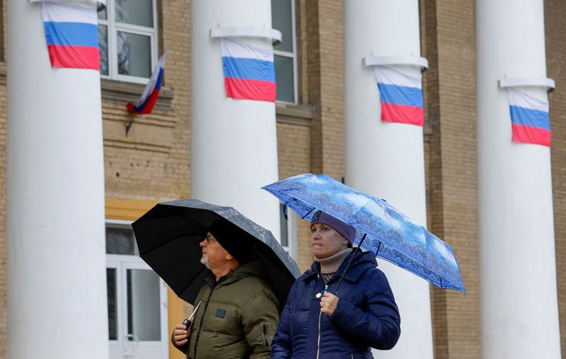 &copy; Reuters. شخصان يمران بمبنى عليه الأعلام الروسية في ميليتوبول يوم 27 نوفمبر تشرين الثاني 2022. تصوير: ألكسندر إيرموتشينكو - رويترز