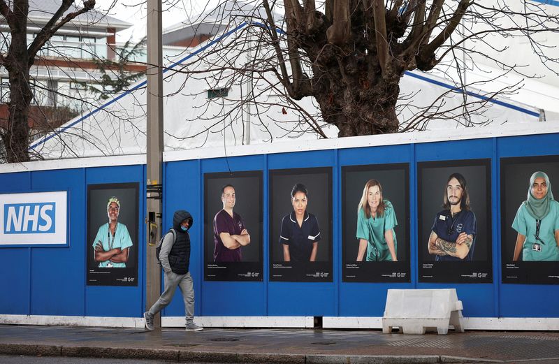 &copy; Reuters. FILE PHOTO: A person walks past images of National Health Service (NHS) workers displayed on hoardings outside a temporary field hospital at St George's Hospital, amid the coronavirus disease (COVID-19) outbreak in London, Britain, January 8, 2022. REUTER