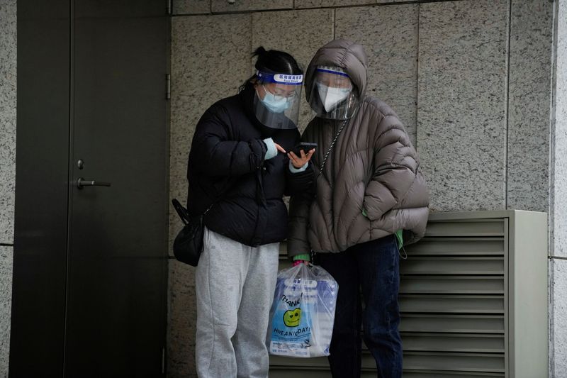 &copy; Reuters. Mujeres con mascarillas y protectores faciales consultan un teléfono en una calle, mientras continúan los brotes de COVID-19 en Shanghái, China, 12 de diciembre de 2022. REUTERS/Aly Song