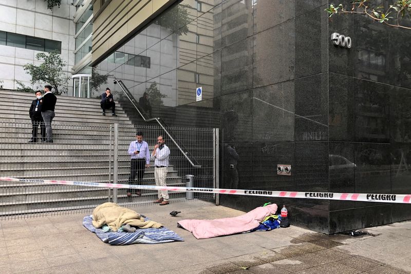 © Reuters. FILE PHOTO: Workers take a break as homeless people sleep behind barricade tape outside an office building in downtown Santiago, Chile, February 16, 2021. REUTERS/Ivan Alvarado/File Photo