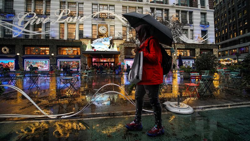 © Reuters. A man walks under the rain with his shopping bags as people visit a department store during the holiday season in New York City, U.S., December 15, 2022. REUTERS/Eduardo Munoz