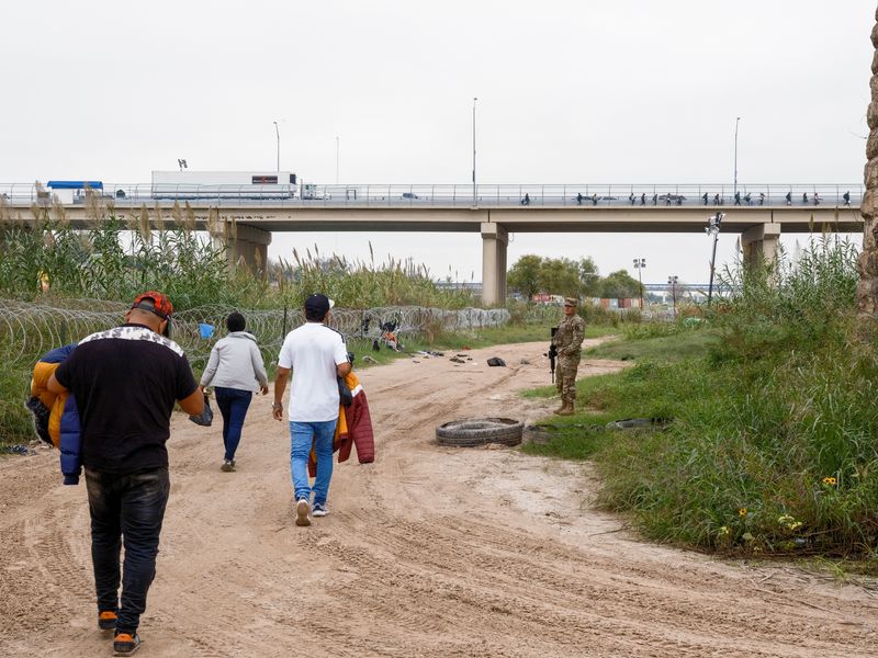 © Reuters. A group of migrants walks towards a border patrol processing area, accompanied by a Texas National Guard member, as U.S. border cities are bracing for an influx of asylum seekers when COVID-19-era Title 42 migration restrictions are set to end, in Eagle Pass, Texas, U.S. December 19, 2022.  REUTERS/Jordan Vonderhaar