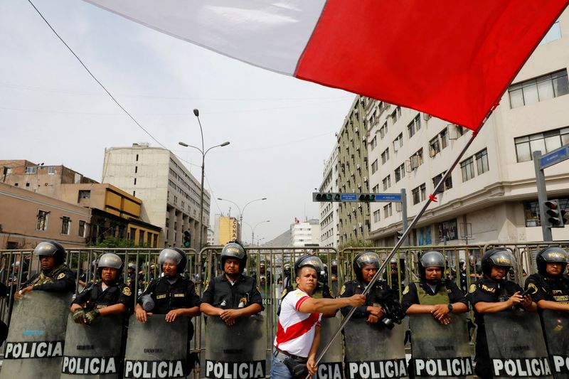 © Reuters. FOTO ARCHIVO: Un hombre agita una bandera mientras policías montan guardia durante una protesta después de que el Congreso aprobara la destitución del presidente Pedro Castillo, en Lima, Perú 7 de diciembre de 2022. REUTERS/Alessandro Cinque/Foto de archivo