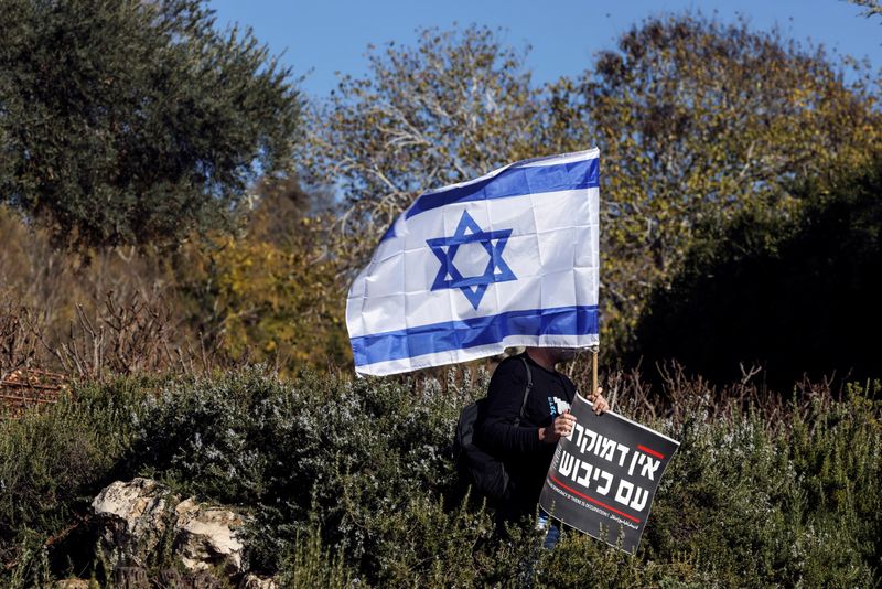 &copy; Reuters. A man holds the national flag of Israel and a sign that says in Hebrew "There is no democracy if there is occupation" at a protest outside the Knesset, Israel's parliament, on the day the new right-wing government is sworn in, with Benjamin Netanyahu as P