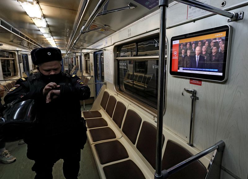 © Reuters. A police officer stands in front of a screen broadcasting Russian President Vladimir Putin's annual New Year address to the nation, in a subway train in Moscow, Russia December 31, 2022. REUTERS/Shamil Zhumatov