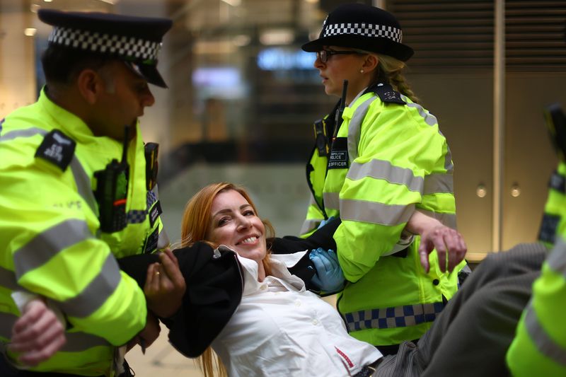 © Reuters. A detained Extinction Rebellion activist, who glued herself to the reception desk earlier, smiles as she is carried out of the building by police during a protest at Shell's headquarters in London, Britain, April 13, 2022. REUTERS/Hannah McKay