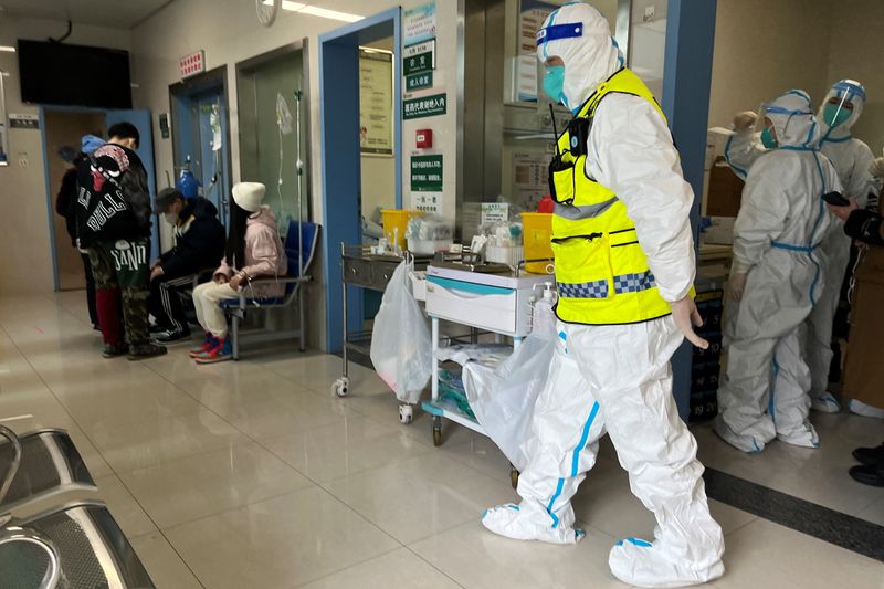 &copy; Reuters. أحد أفراد الأمن يرتدي بدلة واقية بينما يقدم عمال طبيون الرعاية الطبية لمرضى بقسم الحميات في مستشفى تعالج مرضى كوفيد-19 بمدينة ووهان الصينية 