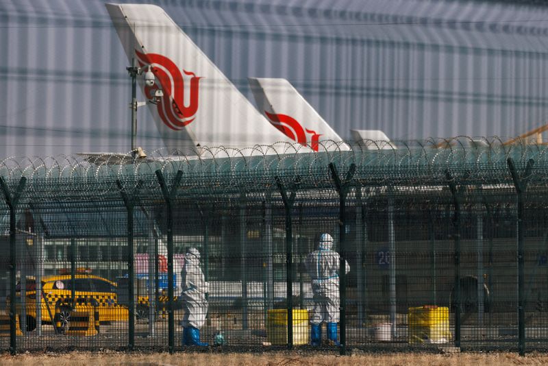 &copy; Reuters. عمال يرتدون بدلات واقية يقفون بالقرب من طائرات الخطوط الجوية الصينية في مطار بكين الدولي يوم الجمعة. تصوير: توماس بيتر - رويترز.