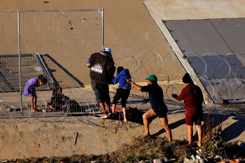 &copy; Reuters. Migrantes en busca de asilo intentan cruzar un alambre de púas que fue colocado por miembros de la Guardia Nacional de Texas en las orillas del río Bravo, frontera entre Estados Unidos y México, visto desde Ciudad Juárez, México. 7 de enero de 2023. 