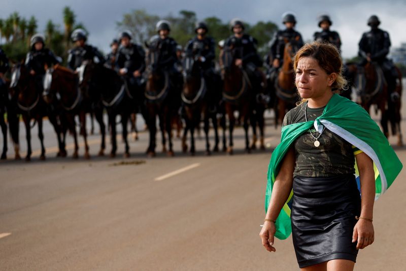 &copy; Reuters. Manifestante bolsonarista caminha em frente a membros de força de segurança em acampamento no entorno de QG do Exército, em Brasília
09/01/2023
REUTERS/Amanda Perobelli