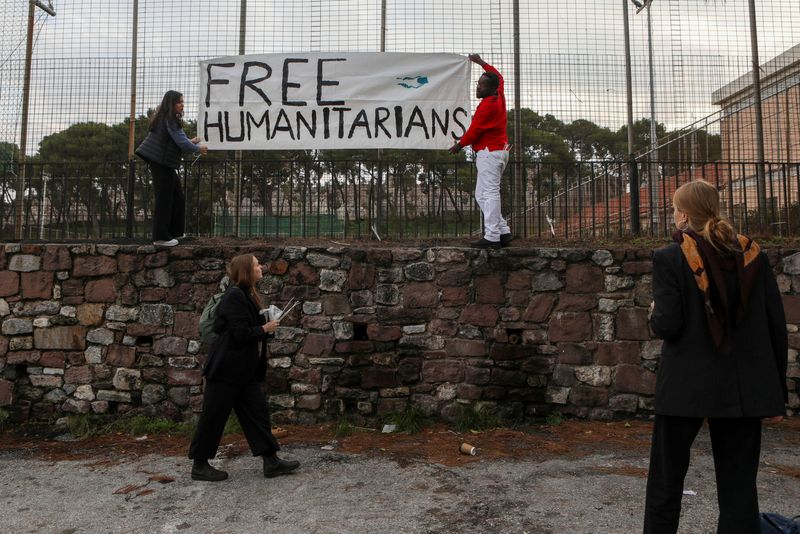 &copy; Reuters. أشخاص يضعون لافتة تأييد أمام محكمة يحاكم بها عمال إغاثة بتهمة إنقاذ لاجئين في جزيرة ليسبوس اليونانية يوم الجمعة. تصوير: إلياس ماركو - رويترز.