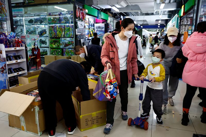 © Reuters. A woman and a child walk past workers sorting toys at a shopping mall in Beijing, China January 11, 2023. REUTERS/Tingshu Wang