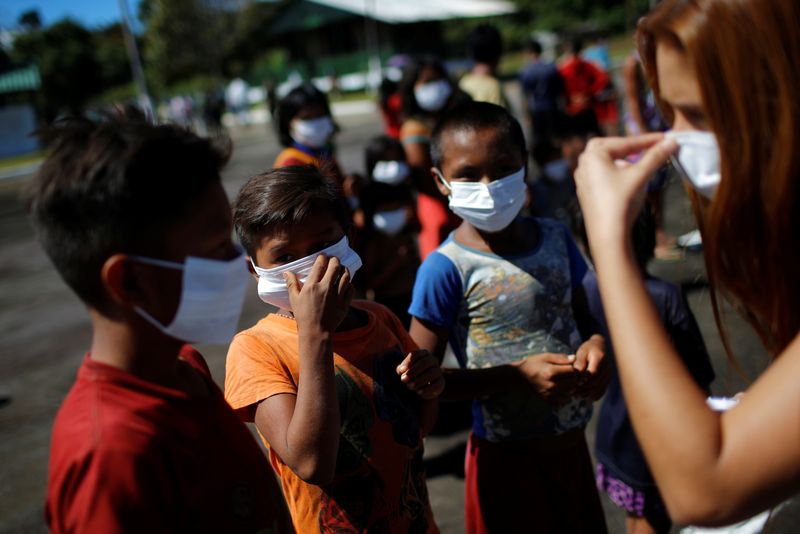 &copy; Reuters. إحدى العاملات الطبيات تساعد أطفالا من عرقية يانومامي وهم السكان الأصليون في البرازيل على وضع كمامات واقية في ولاية رورايما بسبب تفشي فيروس 