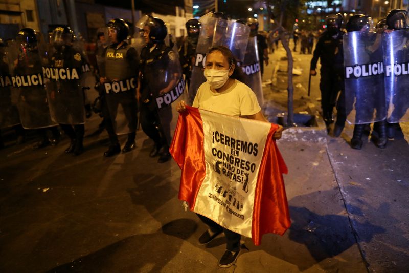 © Reuters. A demonstrator holds a flag in front of riot police officers standing guard during a protest to demand Peru's President Dina Boluarte to step down, in Lima, Peru, January 31, 2023. REUTERS/Sebastian Castaneda