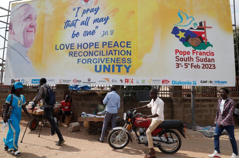 &copy; Reuters. أشخاص يسيرون بالقرب من لافتة تحمل صورة بابا الفاتيكان فرنسيس في إطار التحضيرات لزيارته المرتقبة لجنوب السودان بجوبا في الأول من فبراير 2023. 