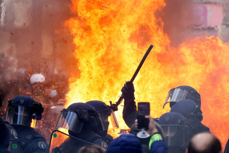 © Reuters. Flames from a fire rise behind law enforcement officers during a demonstration against the French government's pension reform plan as part of the fourth day of national protests, in Paris, France, February 11, 2023. REUTERS/Yves Herman
