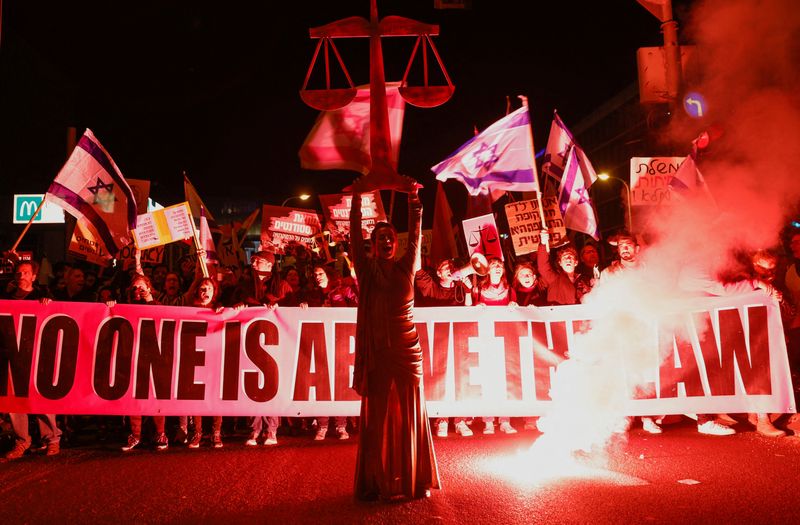 © Reuters. أشخاص يحملون لافتة خلال مظاهرة مناهضة لحكومة رئيس الوزراء الإسرائيلي بنيامين نتنياهو اليمينية وخطط الإصلاح القضائي المقترحة في تل أبيب يوم السبت. تصوير: عمير كوهين - رويترز.