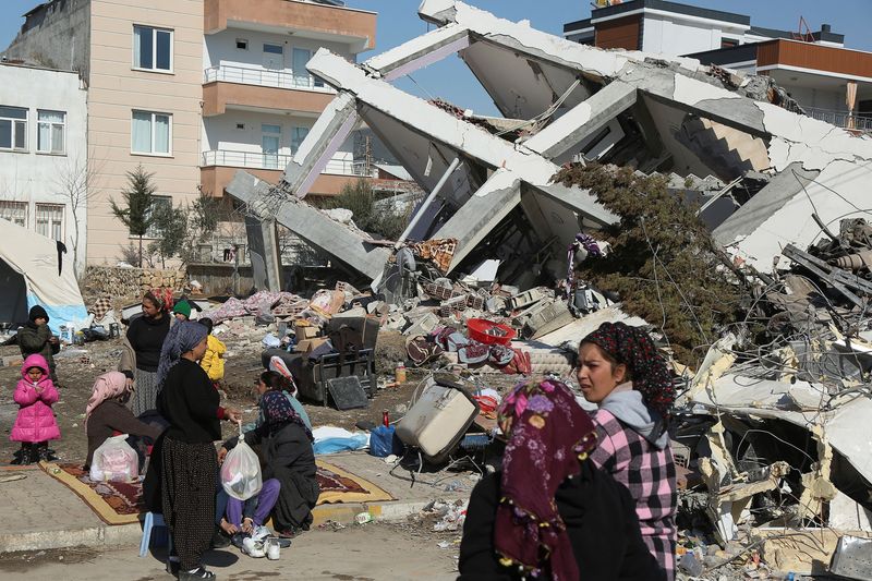 &copy; Reuters. FOTO DE ARCHIVO. Personas sentadas y de pie cerca de un edificio derrumbado, tras el mortífero terremoto, en Adiyaman, Turquía. 12 de febrero de 2023. REUTERS/Sertac Kayar