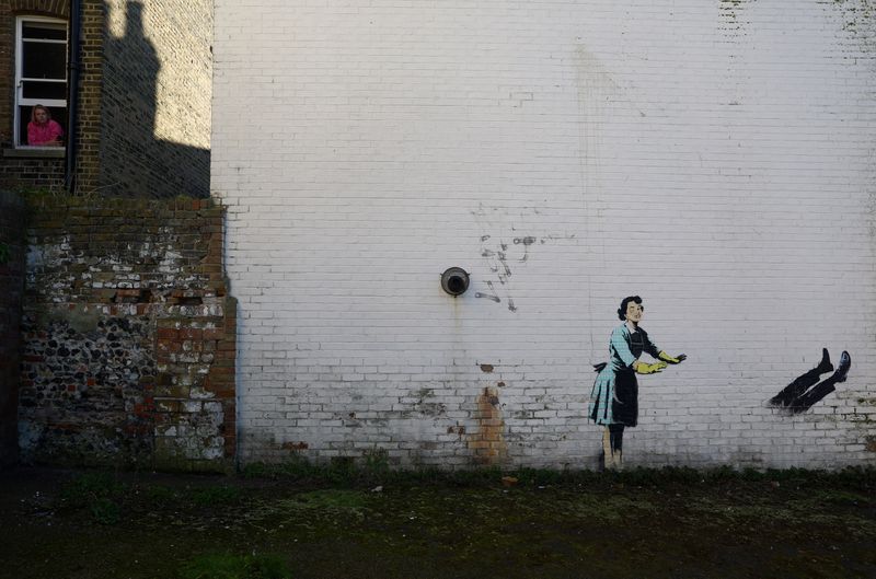 &copy; Reuters. سيدة تنظر من النافذة على لوحة جدارية تصور ربة منزل في الخمسينيات بعين منتفخة وتدفع برجل من صنع فنان الشارع البريطاني بانكسي لتصوير العنف ضد 