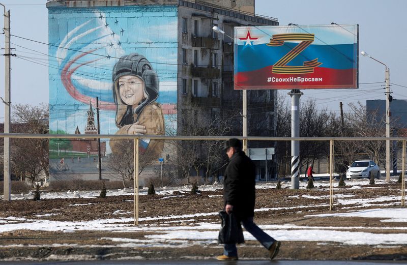 &copy; Reuters. شخص يسير بالقرب من لافتة عليها رمز لدعم القوات المسلحة الروسية في حملتها العسكرية على أوكرانيا في بلدة بشبه جزيرة القرم وعبارة تقول "نحن لا 