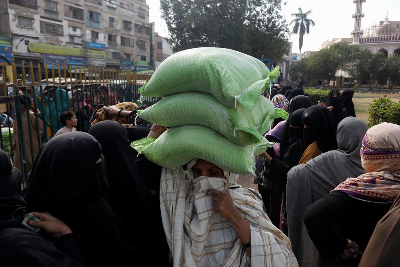 &copy; Reuters. FILE PHOTO: A woman carries sacks of flour on her head, purchased from a truck at subsidised rates, while others stand in queue in Karachi, Pakistan January 11, 2023. REUTERS/Akhtar Soomro