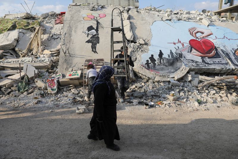 &copy; Reuters. امرأة تمر أمام رسم فني يغطي أنقاض مبان لحق بها الدمار في بلدة جنداريس التي تسيطر عليها المعارضة في سوريا في أعقاب الزلزال المدمر في هذه الصو