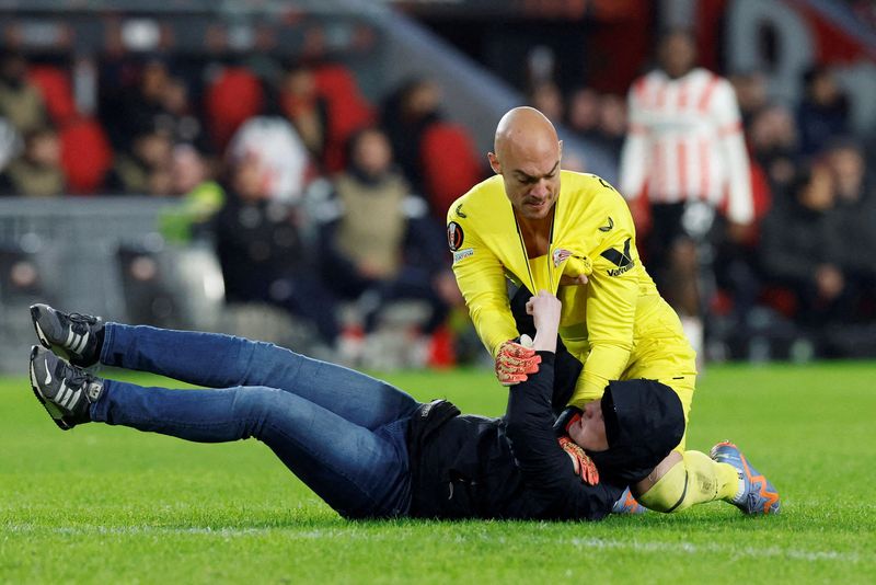 &copy; Reuters. Soccer Football - Europa League - Play-Off Second Leg - PSV Eindhoven v Sevilla - Philips Stadion, Eindhoven, Netherlands - February 23, 2023 Pitch invader clashes with Sevilla's Marko Dmitrovic REUTERS/Piroschka Van De Wouw 