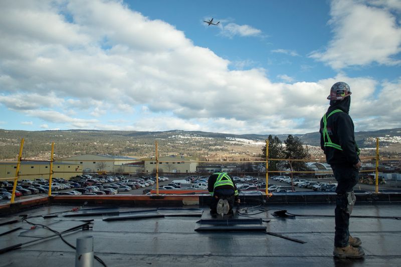 © Reuters. Roofer Max Gordon of TRS Building Envelopes and colleague install flat roofing as a plane passes overhead, at the childcare facility under construction at YLW Kelowna International Airport in Kelowna, British Columbia, Canada, February 14, 2023.  REUTERS/Artur Gajda