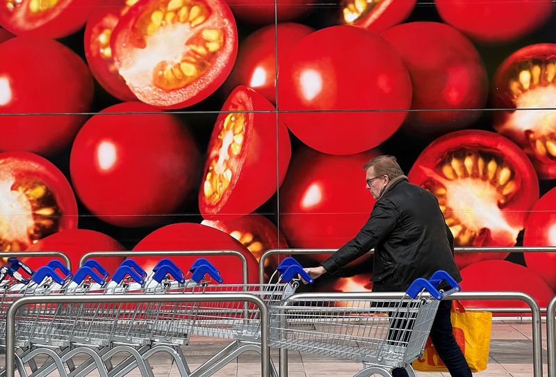 © Reuters. FILE PHOTO: A shopper walks next to a photographic depiction of tomatoes on a Tesco supermarket as Britain experiences a seasonal shortage of some fruit and vegetables, in London, Britain, February 26, 2023. REUTERS/Toby Melville