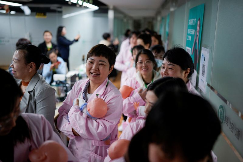 &copy; Reuters. Women holding plastic baby dolls, wait to enter a classroom before a nursing skills class for confinement carers, at Yipeitong training centre in Shanghai, China March 2, 2023. REUTERS/Aly Song