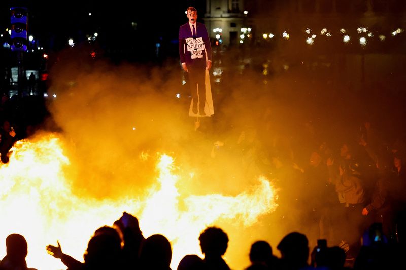 © Reuters. A protester holds a cut-out depicting French President Emmanuel Macron near fire during a demonstration on Place de la Concorde to protest the use by French government of the article 49.3, a special clause in the French Constitution, to push the pensions reform bill through the National Assembly without a vote by lawmakers, in Paris, France, March 17, 2023. REUTERS/Gonzalo Fuentes