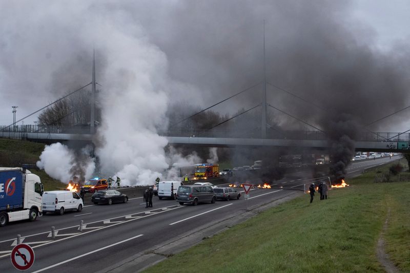 © Reuters. Firefighters and police officers work as smoke rises from burning materials on a highway during a protest against pension reform, in Rennes, France, March 20, 2023, in this image obtained from social media. Twitter @DHR_Damien/via REUTERS