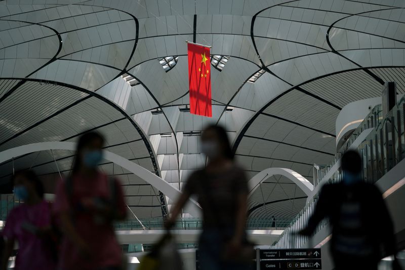 © Reuters. FILE PHOTO: People wearing face masks following the coronavirus disease (COVID-19) outbreak walk under a Chinese flag at Beijing Daxing International Airport in Beijing, China July 24, 2020. REUTERS/Thomas Suen/File Photo