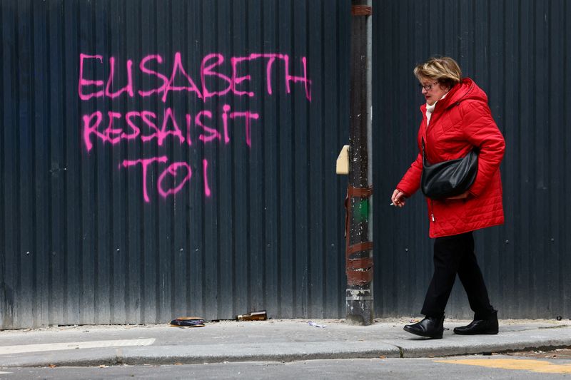 &copy; Reuters. FILE PHOTO: A woman walks past a graffiti reading "Elisabeth, pull yourself together", in reference of French Prime Minister Elisabeth Borne, painted on a metal-sheets wall in a street the day after clashes during protests over French government's pension