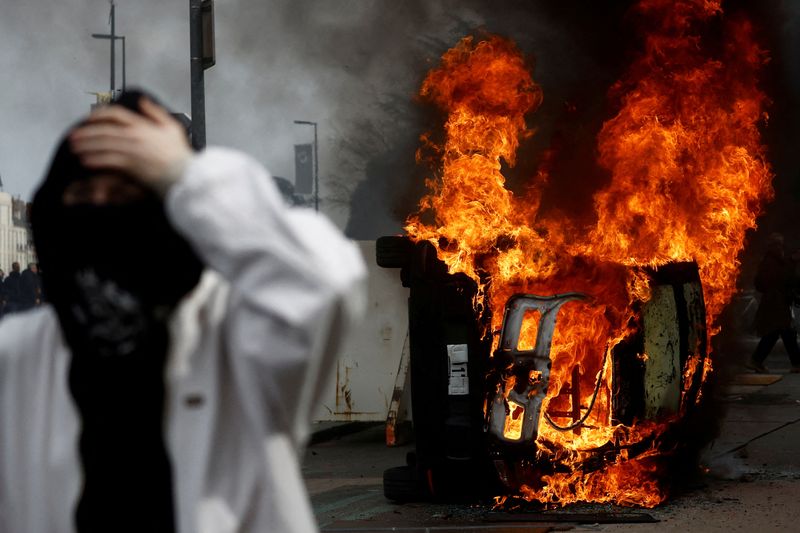 © Reuters. A masked protester stands in front of a burning car during clashes at a demonstration as part of the tenth day of nationwide strikes and protests against French government's pension reform in Nantes, France, March 28, 2023.   REUTERS/Stephane Mahe