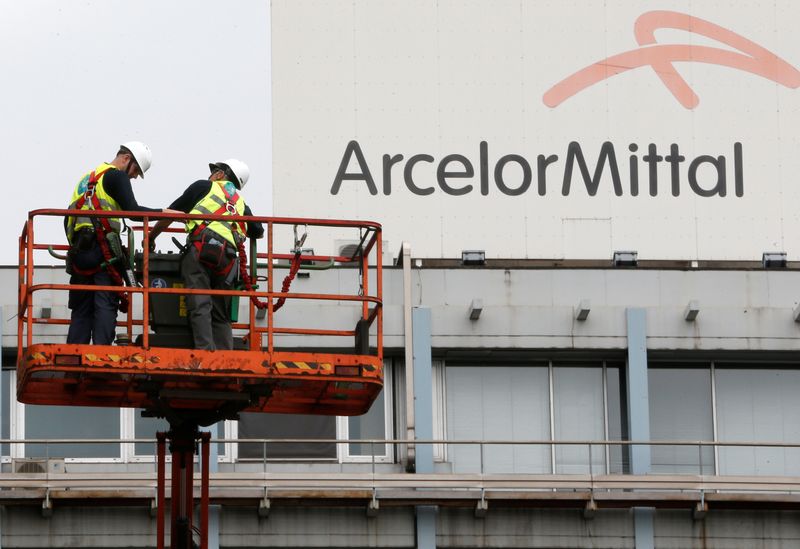 © Reuters. FOTO DE ARCHIVO: Trabajadores de pie cerca del logotipo de ArcelorMittal