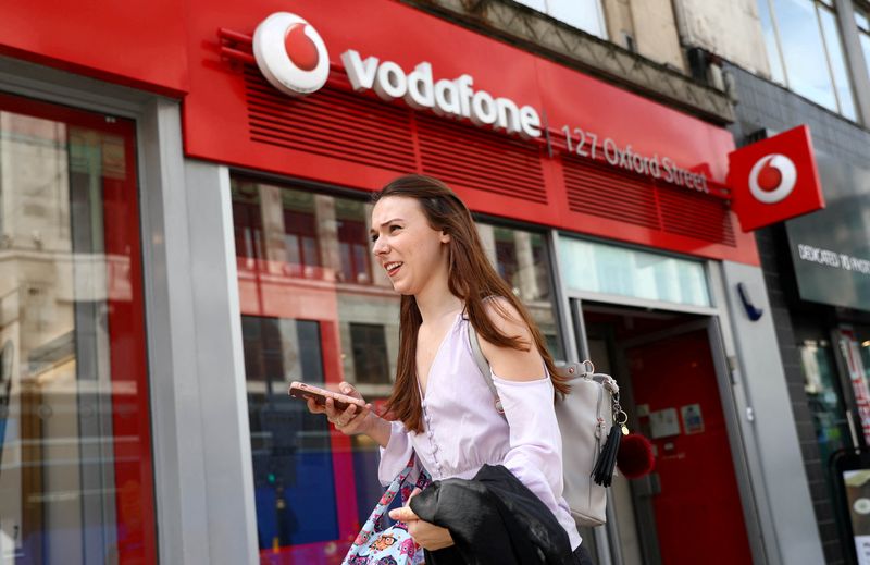 © Reuters. FILE PHOTO: A woman holds a phone as she passes a Vodafone store in London, Britain May 16, 2017. REUTERS/Neil Hall