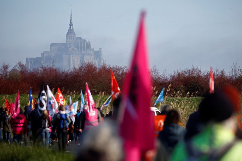 &copy; Reuters. Protesters hold flags of French labour unions as they walk on a country road in Beauvoir towards the Mont Saint-Michel to block the access to the renowned tourist site during a demonstration against French government's pension reform, in the French wester