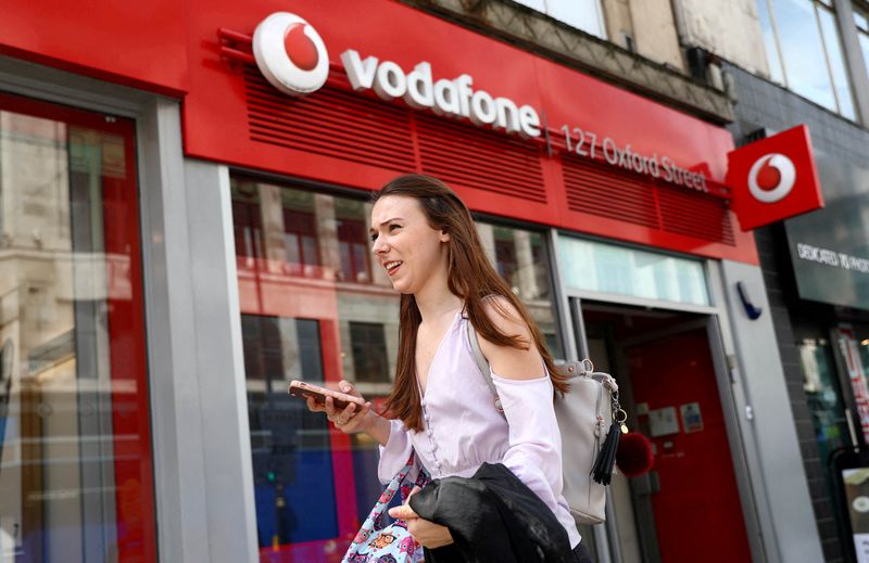&copy; Reuters. FILE PHOTO: A woman holds a phone as she passes a Vodafone store in London, Britain May 16, 2017. REUTERS/Neil Hall