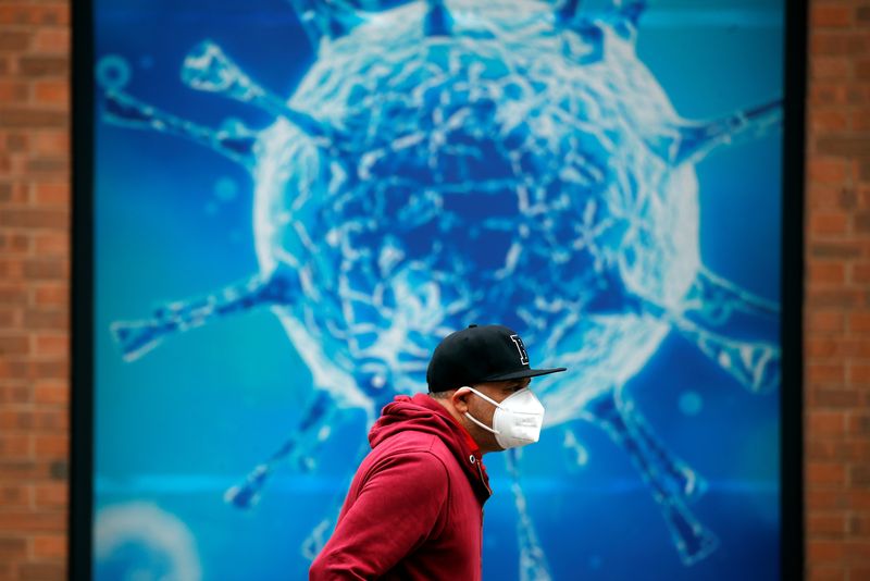&copy; Reuters. FILE PHOTO: A man wearing a protective face mask walks past an illustration of a virus outside a regional science centre, as the city and surrounding areas face local restrictions in an effort to avoid a local lockdown being forced upon the region, amid t