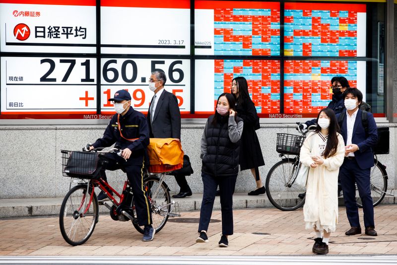 &copy; Reuters. FILE PHOTO: Passersby wait at a crossing in front of an electronic board showing Japan's Nikkei average outside a brokerage, in Tokyo, Japan, March 17, 2023. REUTERS/Androniki Christodoulou