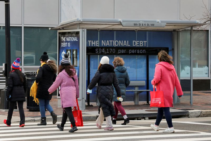 &copy; Reuters. FILE PHOTO: People cross the street next to a bus stop with a sign that shows a U.S. national debt figure, in Washington, U.S., January 20, 2023. REUTERS/Amanda Andrade-Rhoades