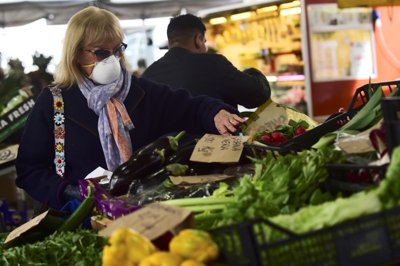 &copy; Reuters. FILE PHOTO: A woman with a protective mask checks vegetable prices at Madama Cristina market, which is virtually deserted after the Italian government imposed a virtual lockdown on a wide swathe of northern Italy, in Turin, Italy March 9, 2020. REUTERS/Ma