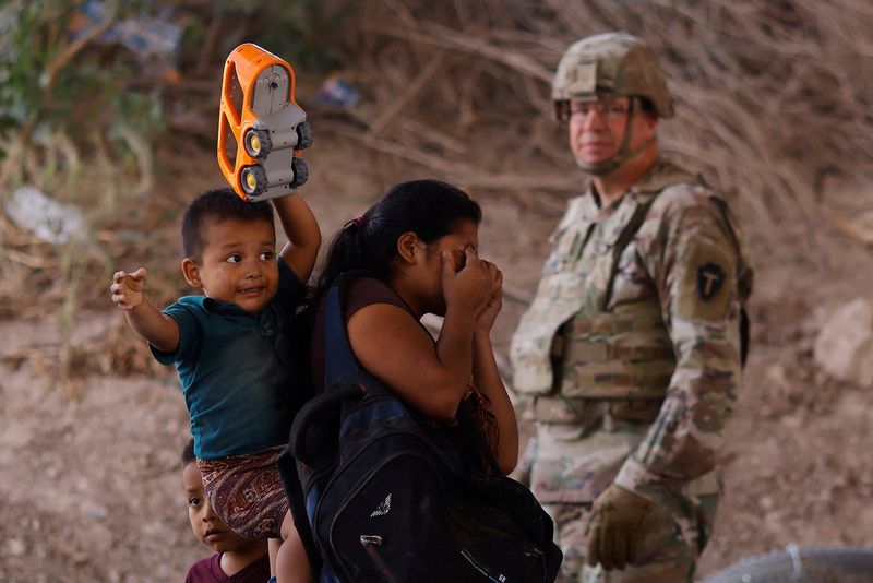 &copy; Reuters. Migrants stand near the Rio Bravo river after crossing the border to, request asylum in the United States, as a member of the Texas Army National Guard stands guard to inhibit migrants crossing, as seen from Ciudad Juarez, Mexico May 13, 2023. REUTERS/Jos
