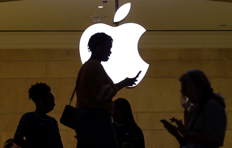 &copy; Reuters. FILE PHOTO: A women uses an iPhone mobile device as she passes a lighted Apple logo at the Apple store at Grand Central Terminal in New York City, U.S., April 14, 2023. REUTERS/Mike Segar