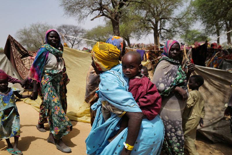 © Reuters. امرأة سودانية تحمل طفلها بينما تسير أمام معسكر مؤقت للاجئين قرب الحدود بين السودان وتشاد يوم 13 مايو أيار 2023 . تصوير: زهرة بن سمرة - رويترز .    
 