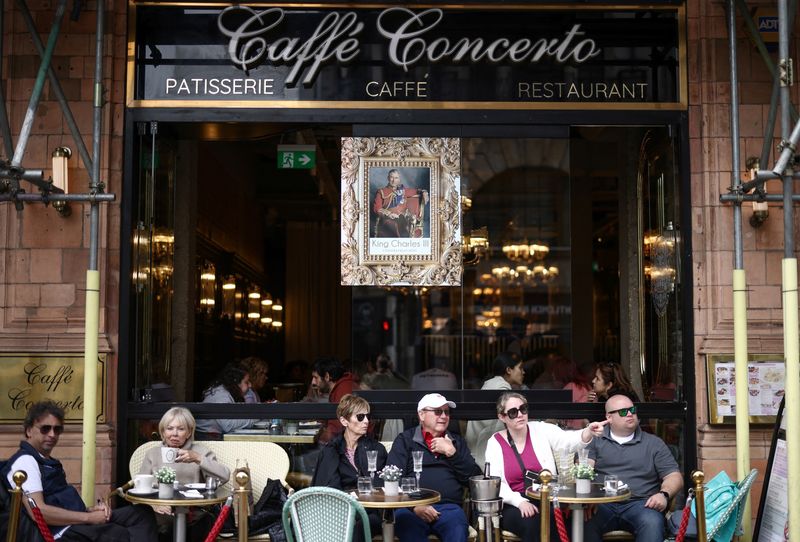 &copy; Reuters. FILE PHOTO: People sit outside a restaurant displaying a portrait of King Charles ahead of the Coronation of King Charles and Camilla, Queen Consort in London, Britain, April 30, 2023. REUTERS/Henry Nicholls