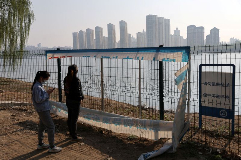 &copy; Reuters. FILE PHOTO: Women wearing face masks following the coronavirus disease (COVID-19) outbreak stand near a fence by a river separating Beijing and Yanjiao in the neighbouring Hebei province, in Beijing, China April 20, 2022. Picture taken April 20, 2022. REU