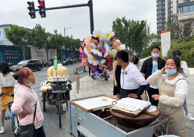 © Reuters. FILE PHOTO: Wang Chunxiang waits for customers as she sells steamed sweet rice cake on a wheel cart among other street vendors in Shanghai, China May 21, 2023. REUTERS/Nicoco Chan