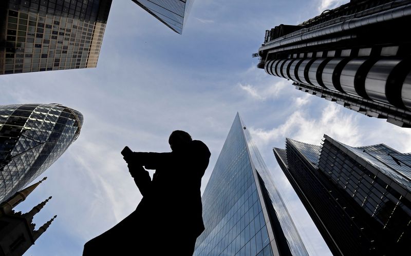 © Reuters. FILE PHOTO: A worker looks at their phone as they walk past The Gherkin, Lloyds, and other office buildings in the City of London, Britain November 13, 2018. REUTERS/Toby Melville